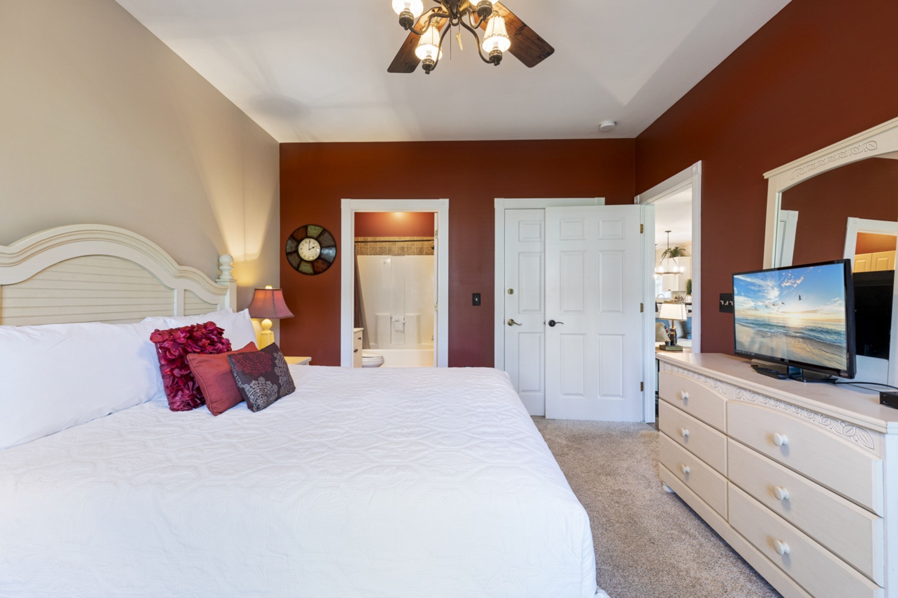 Un dormitorio con cama, cómoda, televisor y puerta que da a un baño.