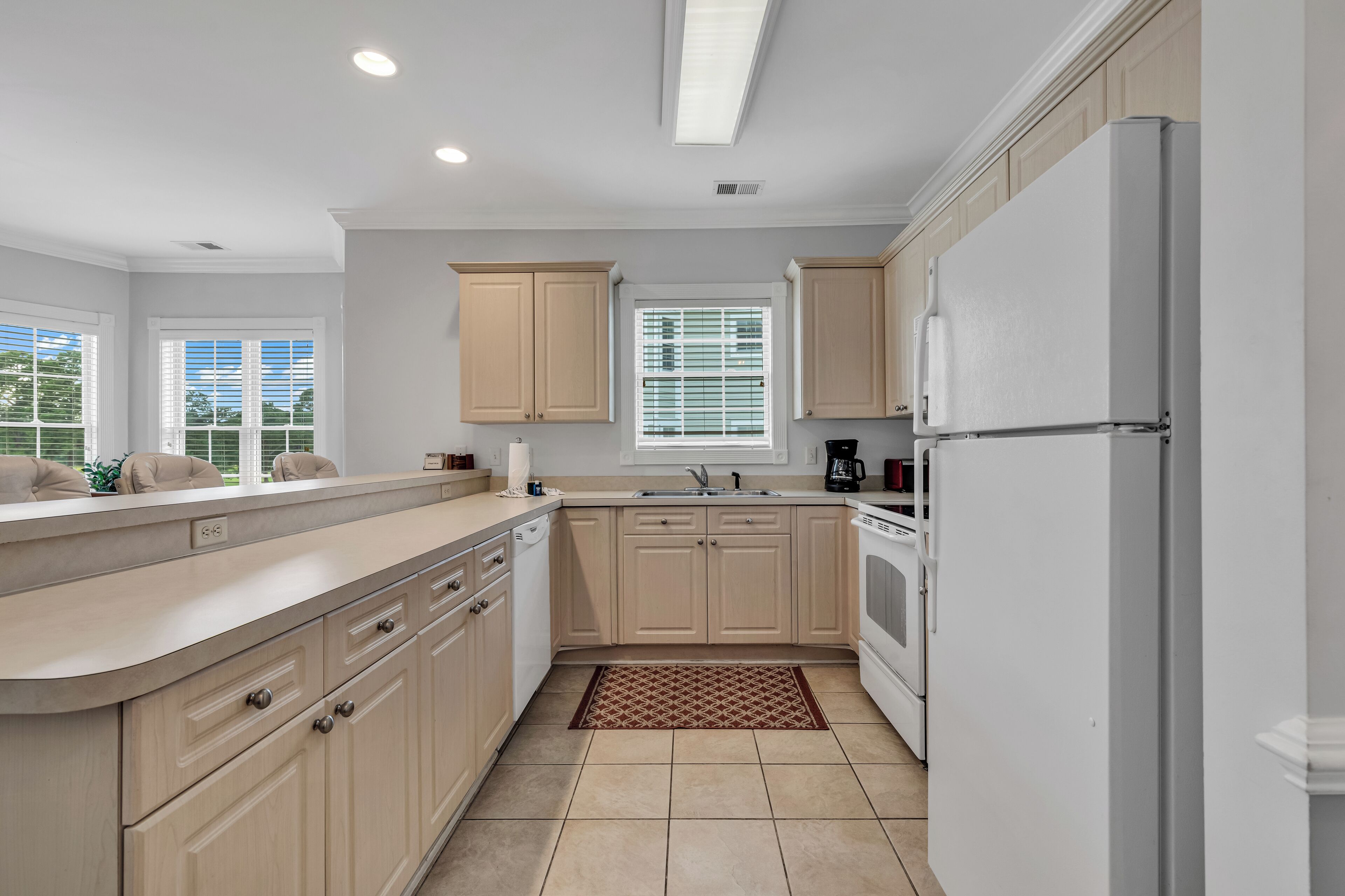 A modern kitchen with light wood cabinets, a white refrigerator, and a window with blinds.