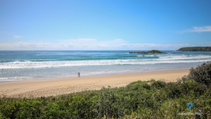 A beach with clear skies, calm waves, and a person walking along the shore.