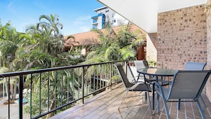 A balcony with a glass table and chairs, a brick wall, and a view of a building and palm trees.