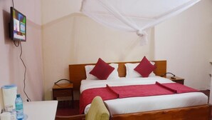 Ein Hotelzimmer mit Bett, Nachttisch, Sessel, Fernseher und Moskitonetz.