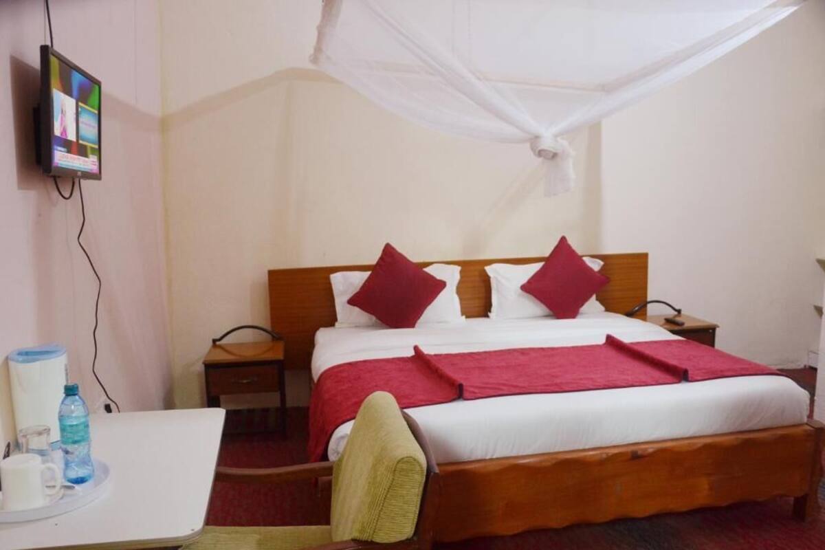 Ein Hotelzimmer mit Bett, Nachttisch, Sessel, Fernseher und Moskitonetz.