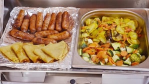 Eine Küchenarbeitsplatte mit einer Platte gebratener Würstchen und einer Schüssel gemischtem Gemüse.