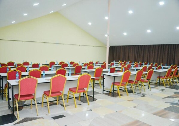 Un salón de conferencias con filas de mesas y sillas, equipado con botellas de agua.