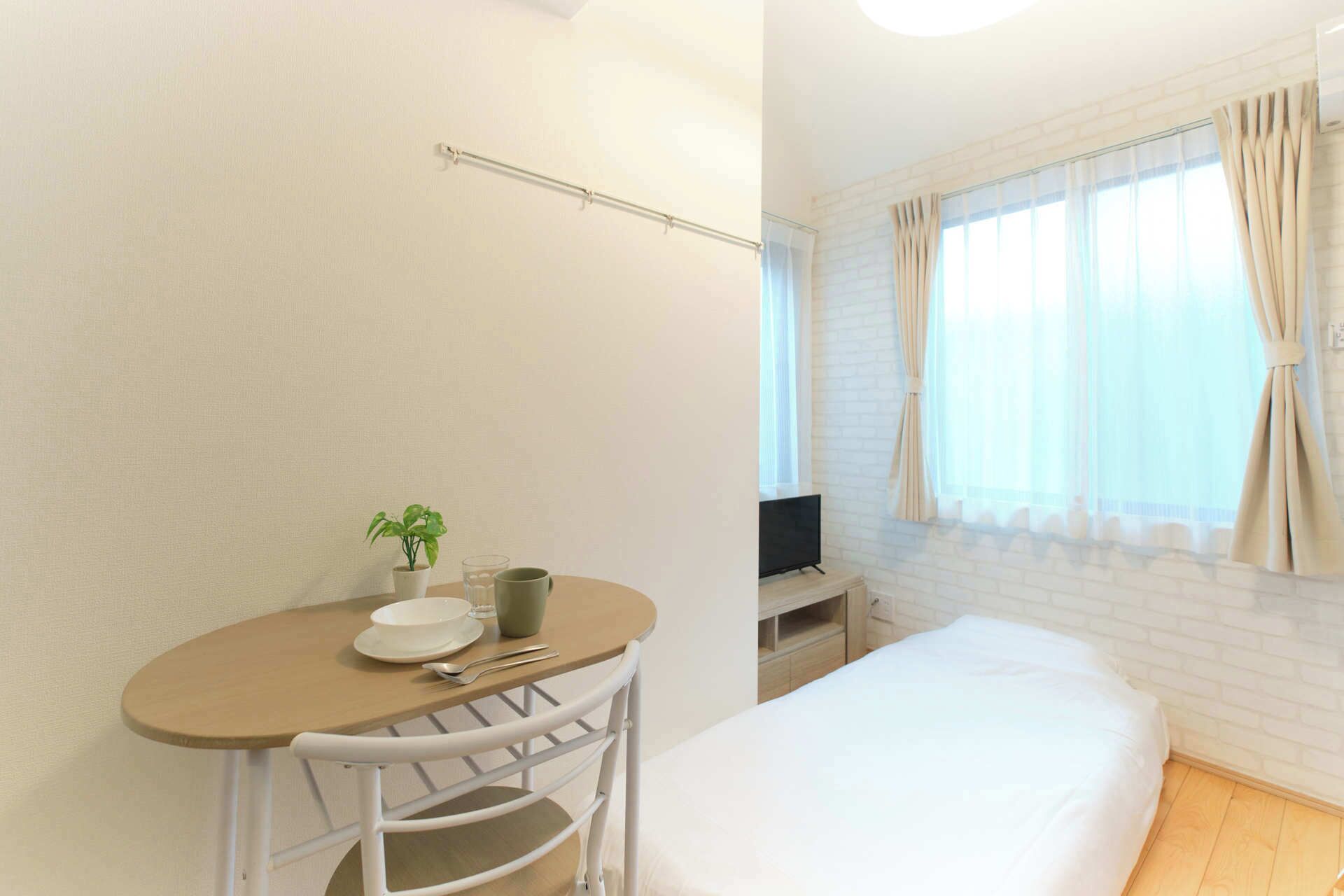 Hotellihuone, jossa on sänky, pieni pöytä, jossa on kasvi, kulho ja kuppi.
