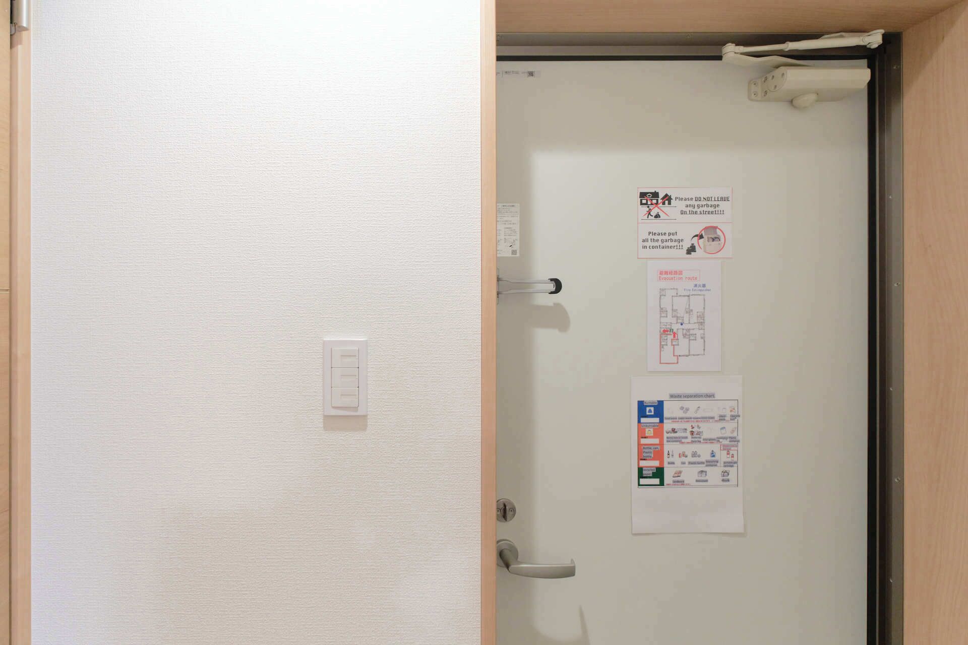 A door with a white interior, a light switch, and several informational posters including a waste separation chart and an evacuation route.