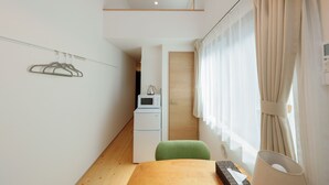 A compact room with a wooden table, a green chair, a microwave, and a small kitchenette. - Nakano Five by Tranova (Tokyo)