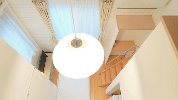 A narrow hallway with a white ceiling, a hanging light fixture, and a wooden staircase. - Nakano Five by Tranova (Tokyo)