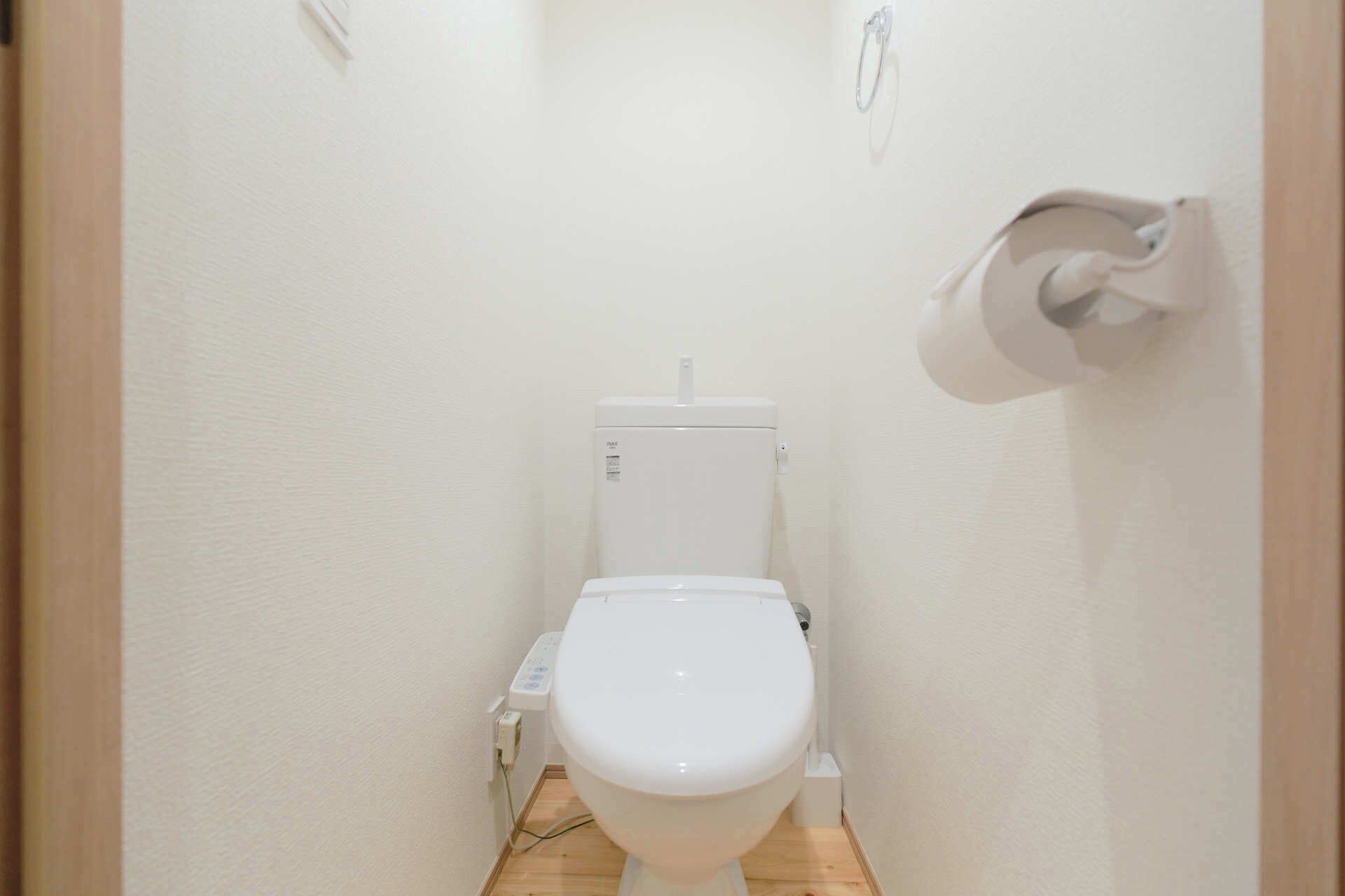 A small, white, standard toilet with a tank and a flush handle on the right.