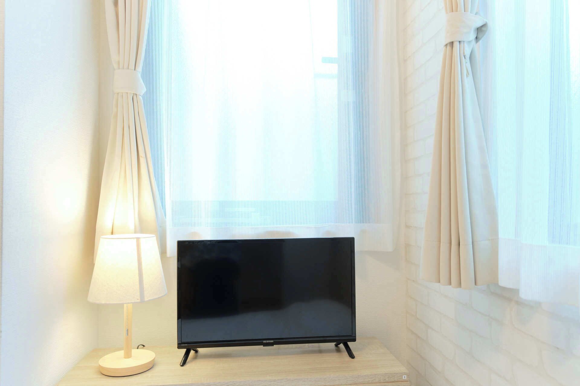 A TV on a wooden stand in a room with white brick walls and sheer curtains.