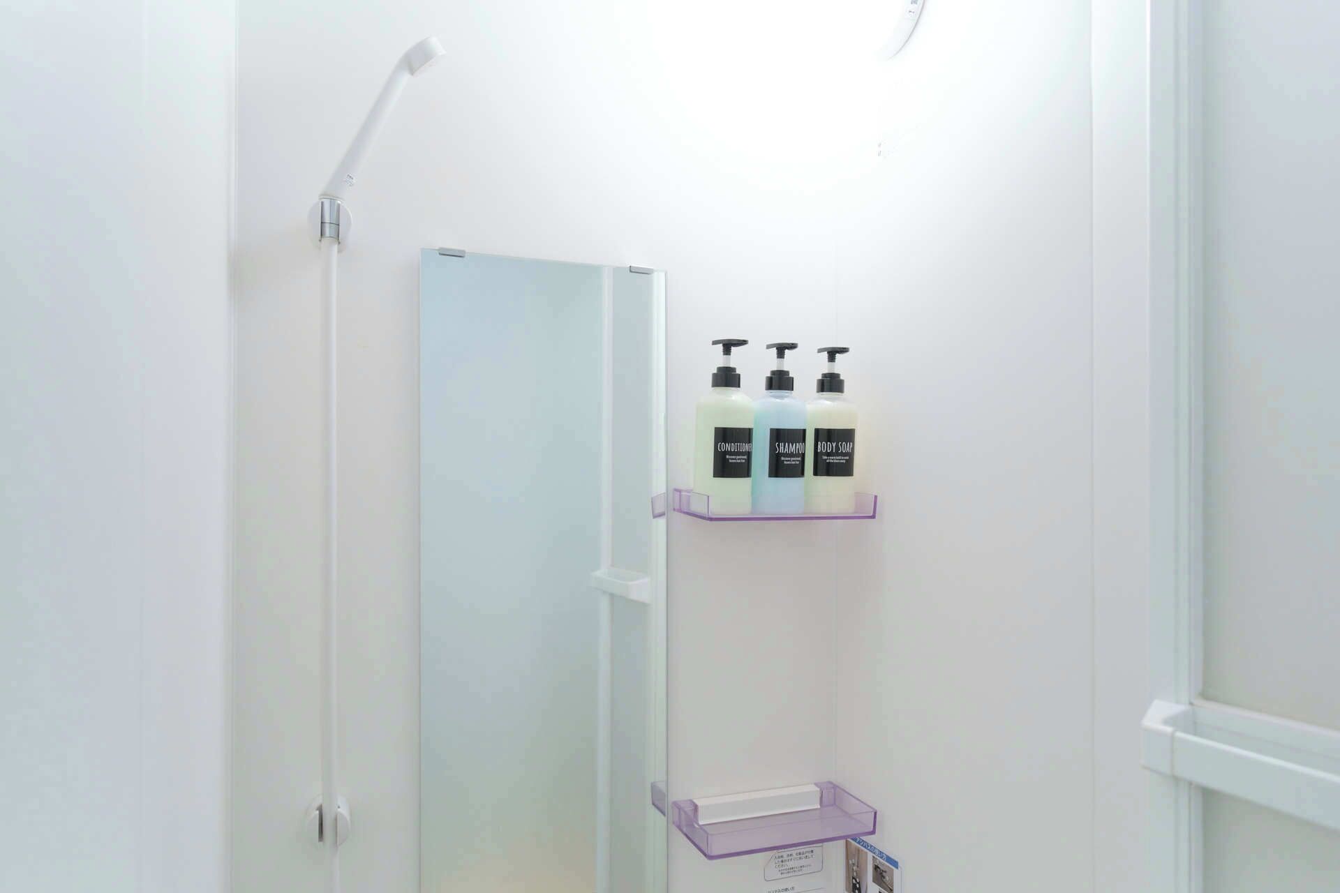 A bathroom with a white door, a shower, and a shelf with three bottles of toiletries.
