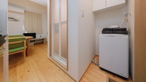 A compact room with a wooden floor, a green chair, a small table, a white refrigerator, and a sliding door. - Nakano Five by Tranova (Tokyo)