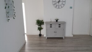 A room with a wooden floor, a white cabinet with drawers, a potted plant, and a wall clock. - The Broadway Rooms  (Leicester)