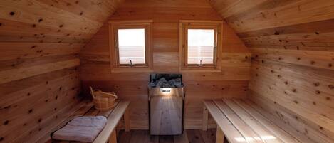 Una cabaña de madera con dos ventanas, un banco y una sauna.