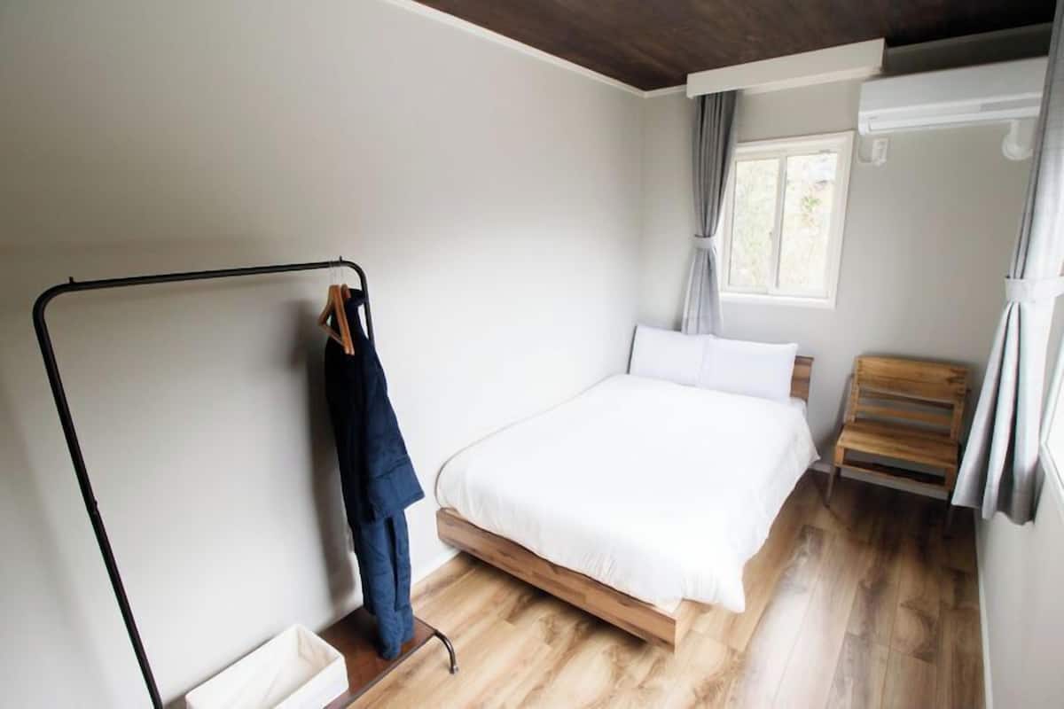 Ein Schlafzimmer mit Bett, Holzboden, einer Kleiderstange und einem Fenster mit Vorhängen.
