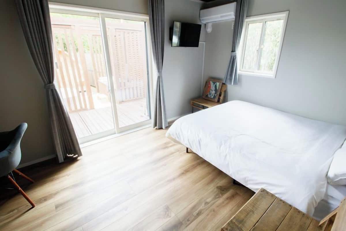 Ein Schlafzimmer mit einem großen Bett, einem Sessel, einem Fernseher und Blick ins Freie.