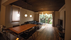 A modern living room with a wooden dining table, black leather sofa, and a large TV. - LOCALINO STAY AOSHIMA (Miyazaki)