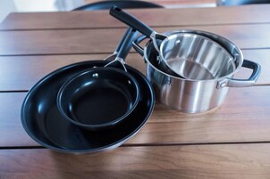 A stainless steel pot with a lid and a black frying pan on a wooden table.