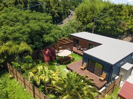 A modern house with a deck, a covered outdoor seating area, and lush greenery surrounding it.