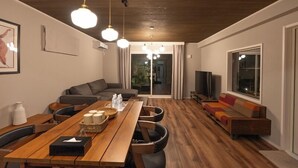 A modern living room with a wooden dining table, leather chairs, a grey sofa, and a TV. - LOCALINO STAY AOSHIMA (Miyazaki)