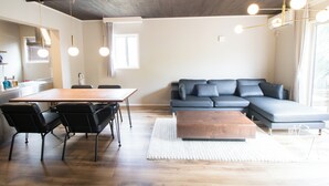 A modern living room with a wooden dining table, black chairs, a grey sectional sofa, a wooden coffee table, and pendant lighting. - LOCALINO STAY AOSHIMA (Miyazaki)