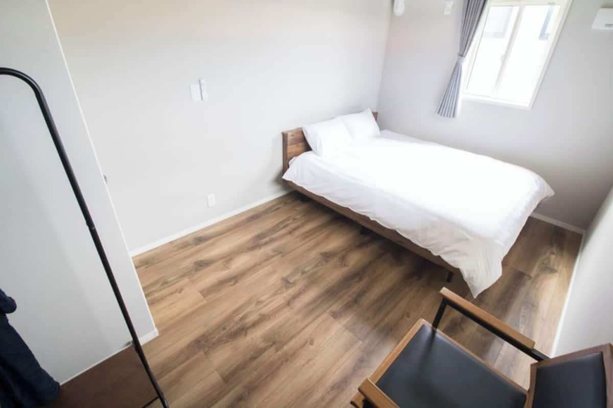 Ein kleines Zimmer mit einem Einzelbett, Holzboden und einem Fenster mit Vorhängen.