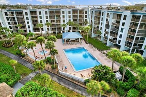 A multi-story hotel with a central swimming pool surrounded by palm trees and lounge chairs. - The Riverside Club - B206 (Marco Island)