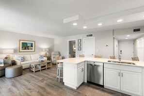 A modern kitchen with white cabinetry, a built-in dishwasher, and a large island with a sink. - The Riverside Club - B206 (Marco Island)