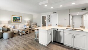 A modern kitchen with white cabinetry, a built-in dishwasher, and a large island with a sink. - The Riverside Club - B206 (Marco Island)