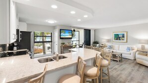 A modern kitchen with a central island, a dining area with a white sofa, and a living room with a white couch. - The Riverside Club - B206 (Marco Island)