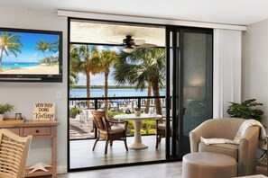 Una habitación con un gran ventanal corredera que da a un balcón con vistas a palmeras y al mar.