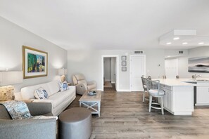 A modern living room with a sofa, a coffee table, and a dining area with a bar. - The Riverside Club - B206 (Marco Island)