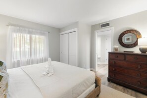 A bedroom with a large bed, a dresser, and a mirror on the wall. - The Riverside Club - B206 (Marco Island)