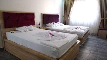 Two wooden beds with white linens and red headboards in a room with a large window and curtains.