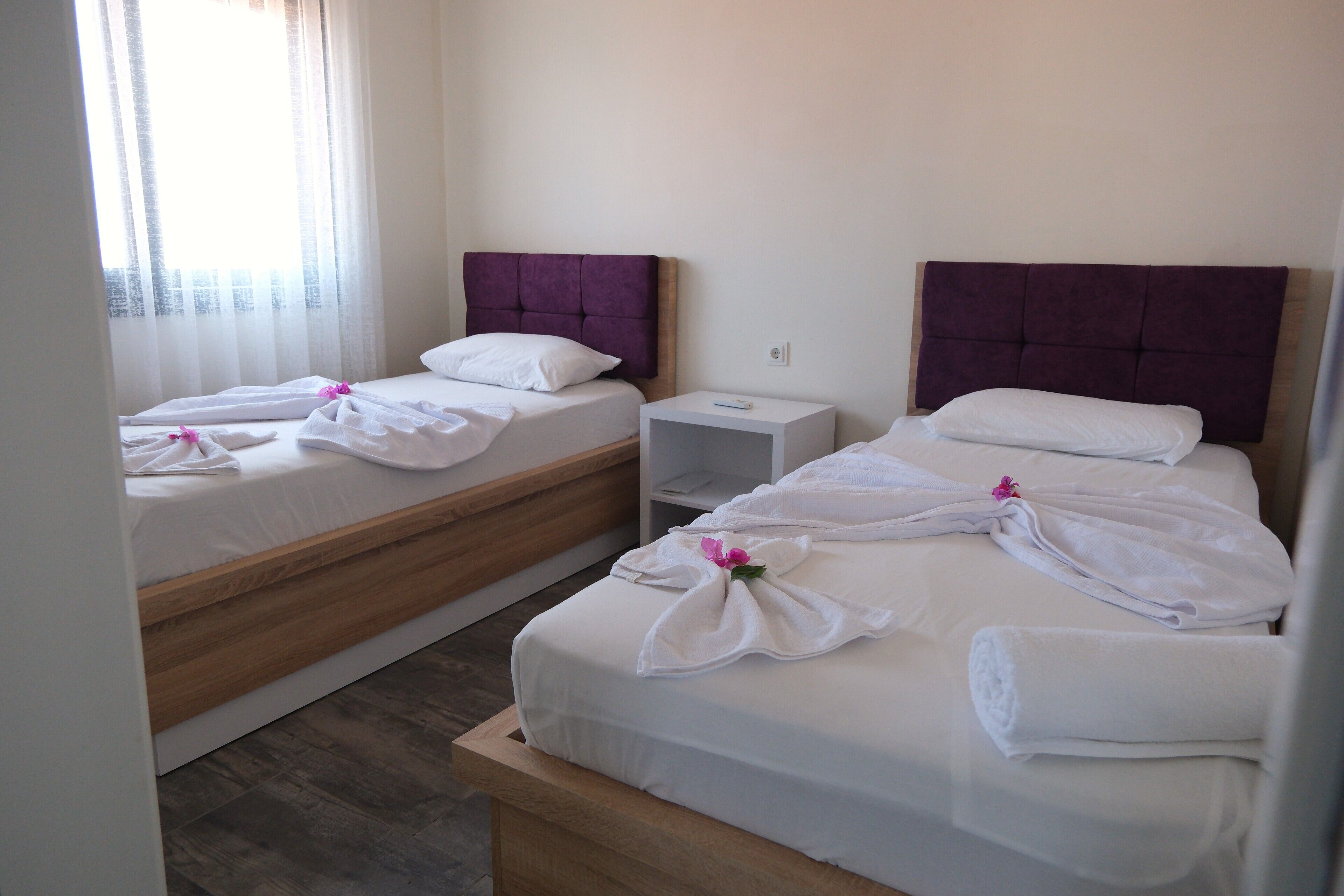 Ein Hotelzimmer mit zwei Betten, jeweils mit Holz Kopfteilen und weißer Bettwäsche. Zwischen den Betten steht ein Nachttisch, und das Zimmer hat eine neutrale Farbgestaltung.