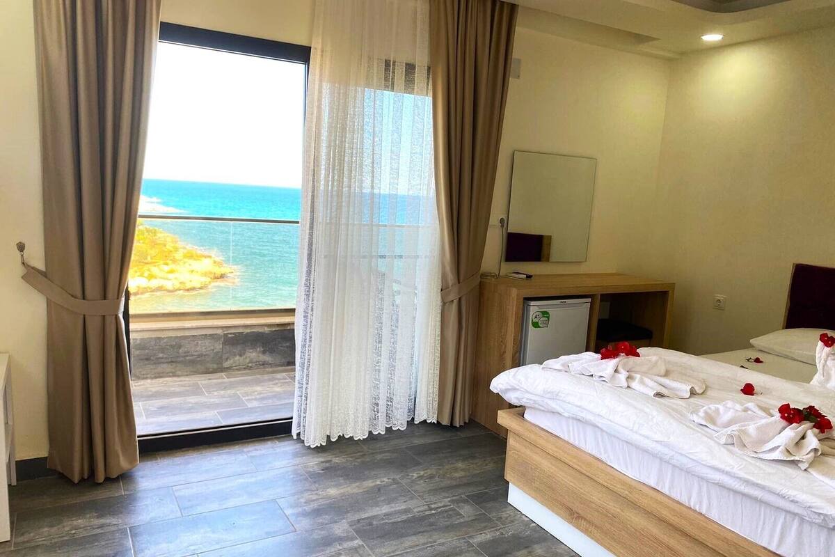 A hotel room with a bed, a small desk, a mirror, and a view of the ocean.