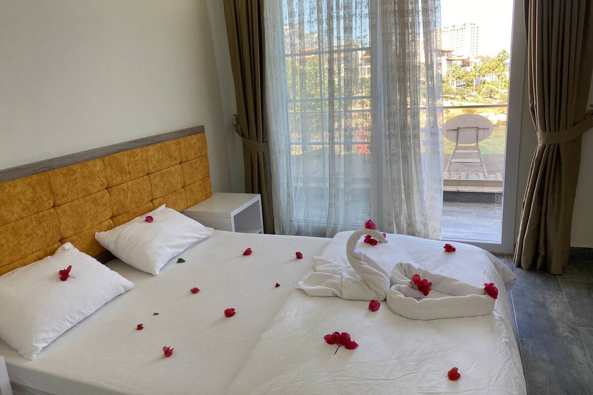 A hotel room with a bed, white bedding, and rose petals.