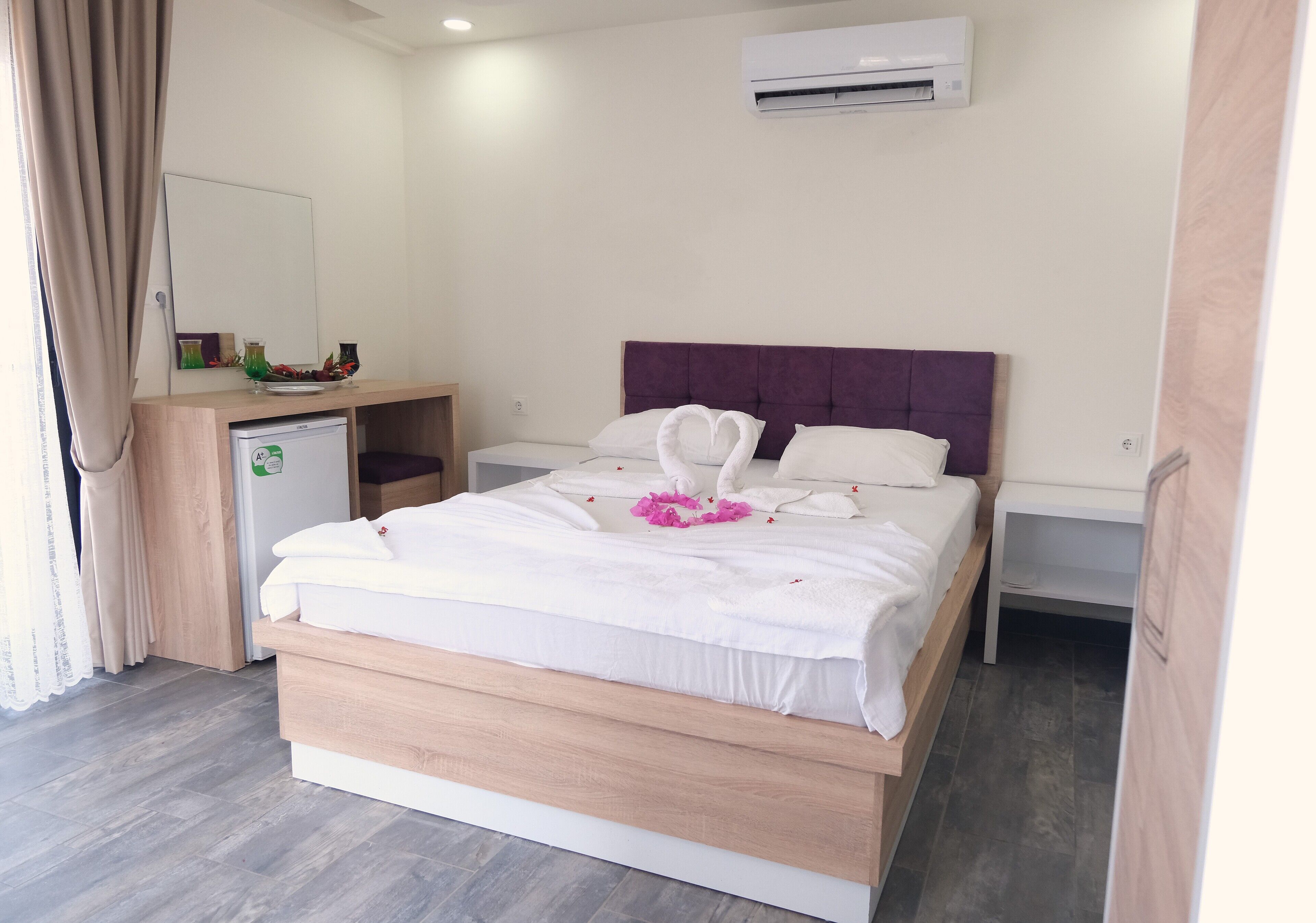 A hotel room with a bed, a small desk, a mirror, and an air conditioning unit.