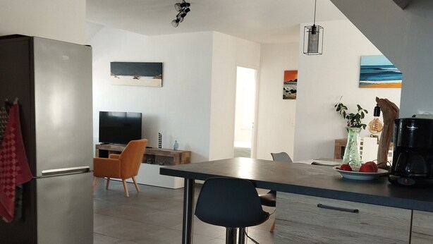 Une cuisine moderne dotée d’un îlot central, de tabourets de bar et d’un coin repas avec un téléviseur.
