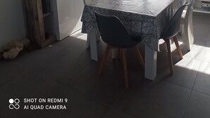 Un coin repas comprenant une table, des chaises, un buffet en bois, un luminaire suspendu, une fenêtre avec des rideaux et un tableau accroché au mur.