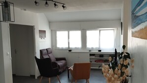 Un espace de vie spacieux comprenant un canapé, des fauteuils, une table à manger et une grande fenêtre laissant entrer la lumière naturelle.