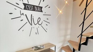 Un interior moderno con un mueble consola de madera, una escalera y una pared con un letrero decorativo.