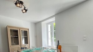 Un comedor con una mesa de madera, sillas blancas y negras, un armario con puertas de cristal y una botella sobre la mesa.