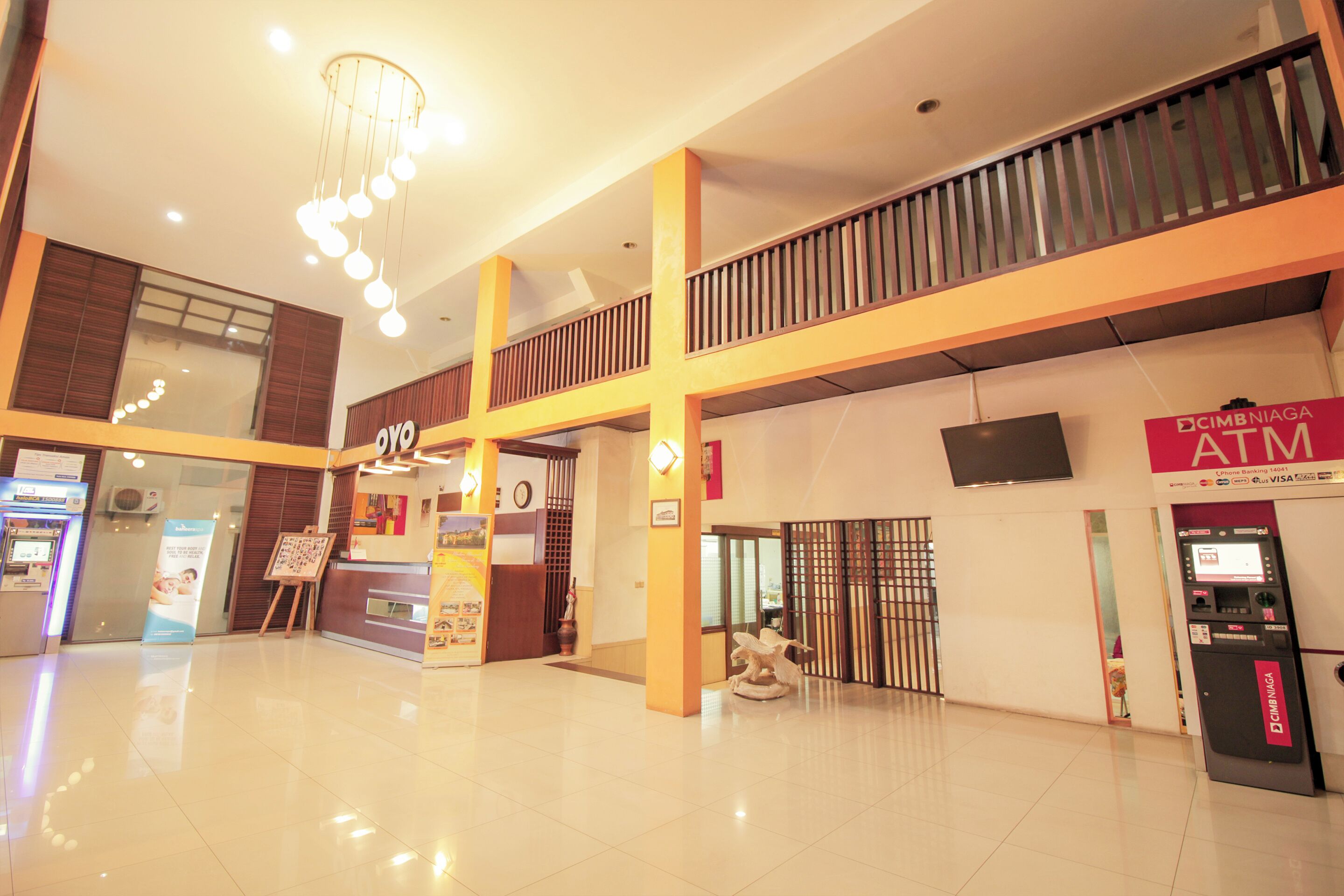 A spacious lobby with a reception desk, an ATM, and a staircase leading to an upper level.