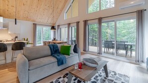 A spacious living area with a high ceiling, large windows, a sofa, a dining table, and a kitchen area. - Le Stockholm - Hot tub and Golf, Shared pool (Shannon)