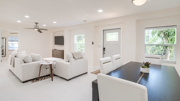 A modern living room with a dark dining table, white sofas, and a ceiling fan.