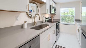 A modern kitchen with white cabinets, gold handles, a stainless steel sink, and a microwave.