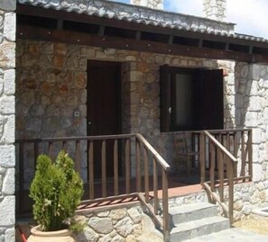A stone building with a wooden porch and a staircase leading to a door.