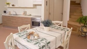 A compact kitchen with white cabinets, a stove, and a sink. There's a dining table with a white tablecloth and chairs. - Your Gorge-side Getaway Modern Villas, Natural Beauty (Platanias)