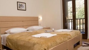 A bedroom with a wooden bed, white pillows, and a tan bedspread. There is a nightstand with a lamp and a framed picture on the wall. - Your Gorge-side Getaway Modern Villas, Natural Beauty (Platanias)